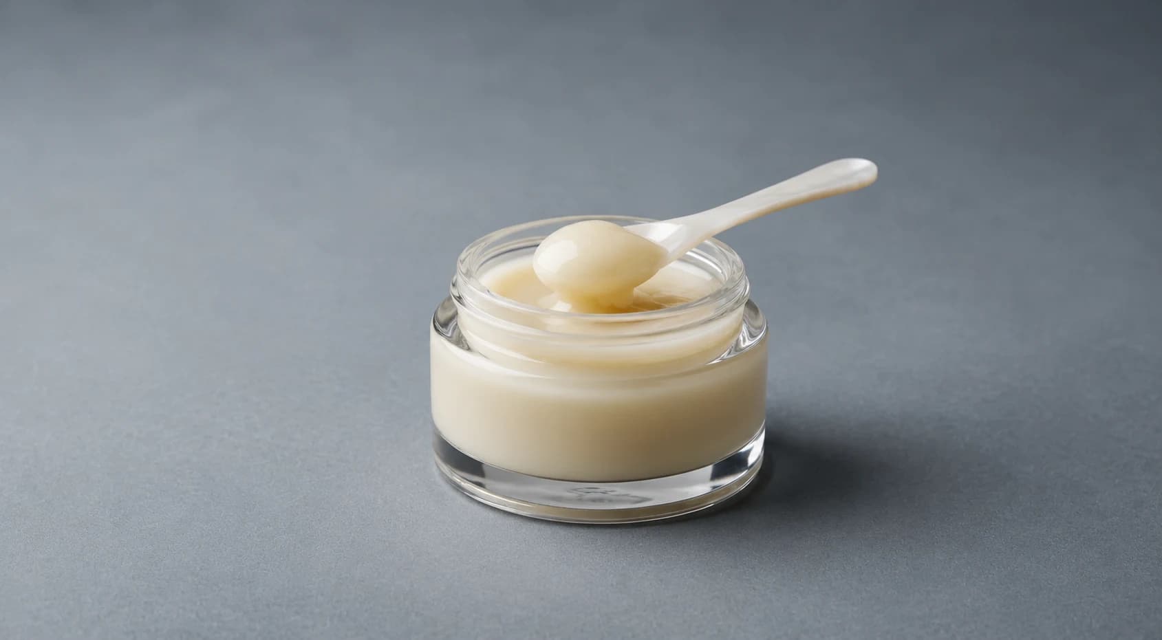 Pale creamy royal jelly in a small glass jar with a spoon lifting a sample